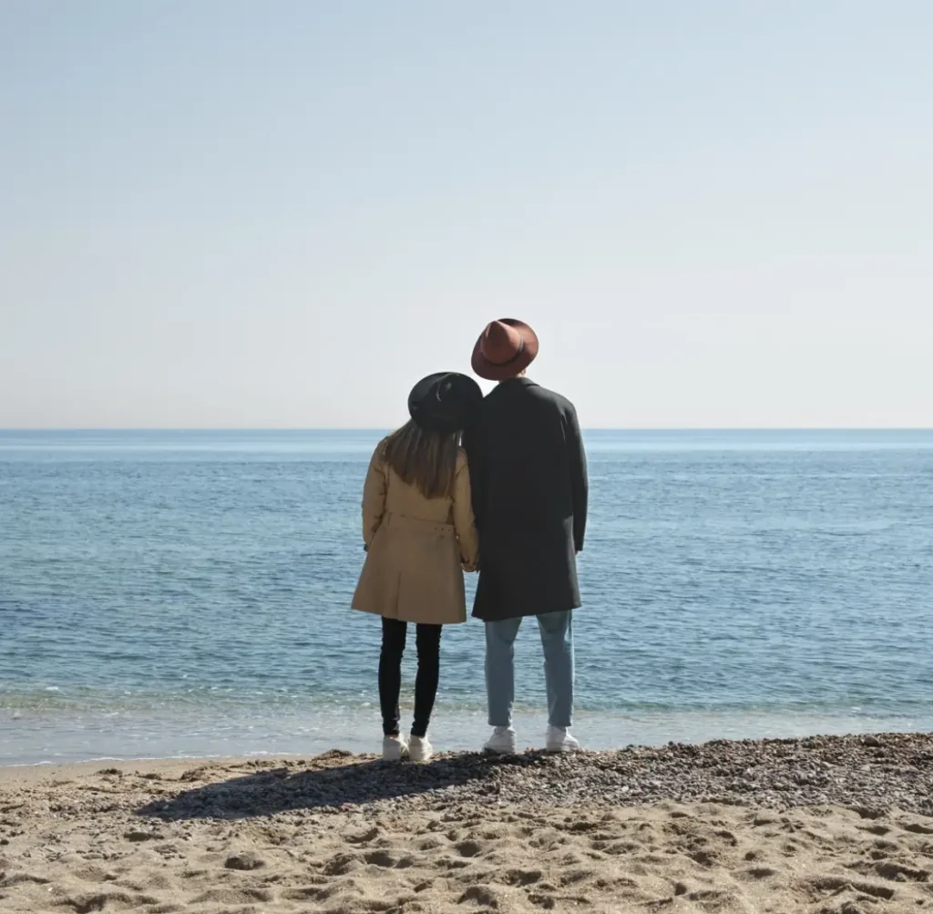 Casal de frente a praia olhando o horizonte. A imagem ilustra o texto de psicoterapia de casal online